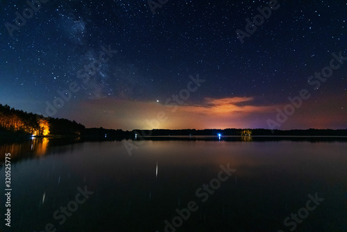 A magical starry night on the river bank with a large tree and a milky way in the sky and falling stars in the summer. 