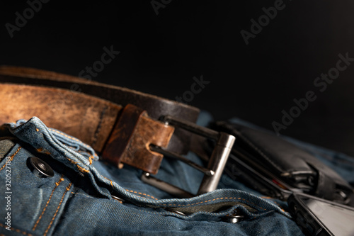 Men's accessories, fashion trends - jeans, a leather belt, an ajar wallet, casually lie on a black background with a blurred depth of field, close-up. Emphasizes the masculinity of a real man.