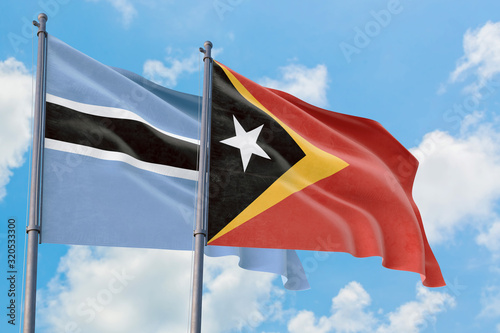 East Timor and Botswana flags waving in the wind against white cloudy blue sky together. Diplomacy concept, international relations.