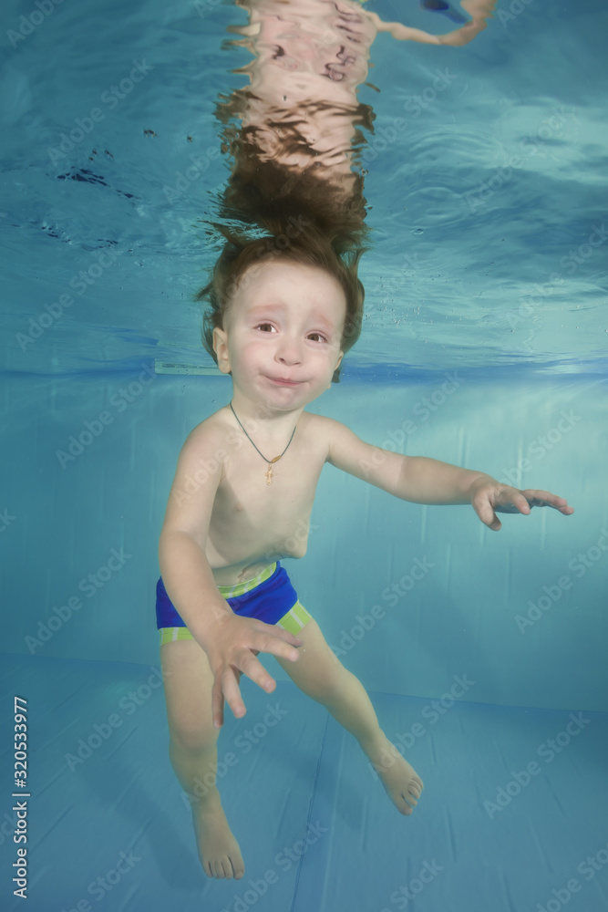 Funny red-haired boy plays with toy underwater in a swimming pool