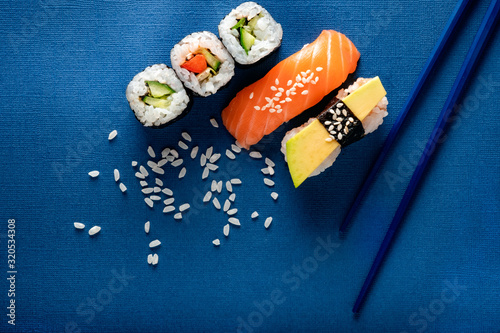 Set of sushi and rolls with salmon, avocado and cucumber on a blue background with chopsticks, top view