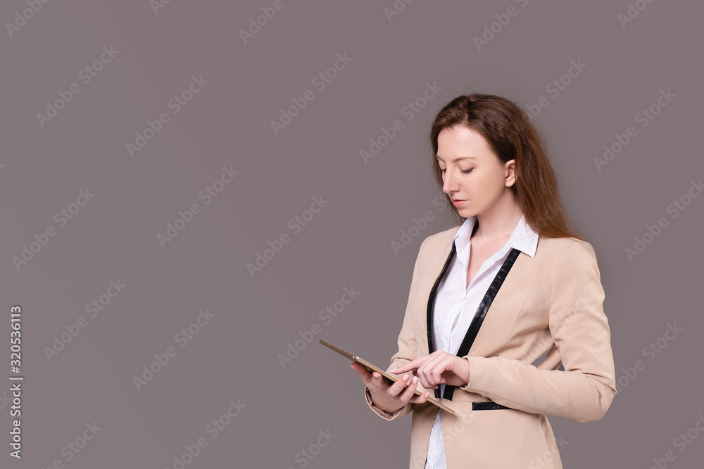 Successful ?aucasian positive elegant businesswoman in a beige jacket and holding a tablet in her hands posing on a purple background. Happy young woman advertises wholesales stores. Advertising space Successful ?aucasian positive elegant businesswoman in a beige jacket and holding a tablet in her hands posing on a purple background. Happy young woman advertises wholesales stores. Advertising space