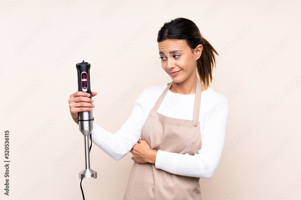 Woman using hand blender over isolated background with sad expression Woman using hand blender over isolated background with sad expression