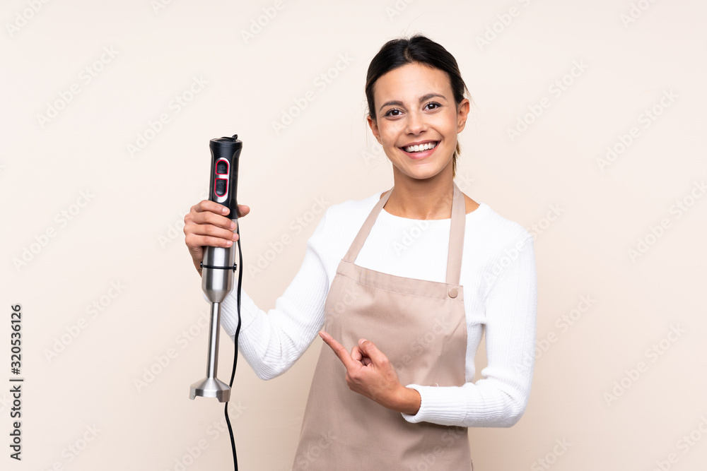 Woman using hand blender over isolated background and pointing it Woman using hand blender over isolated background and pointing it