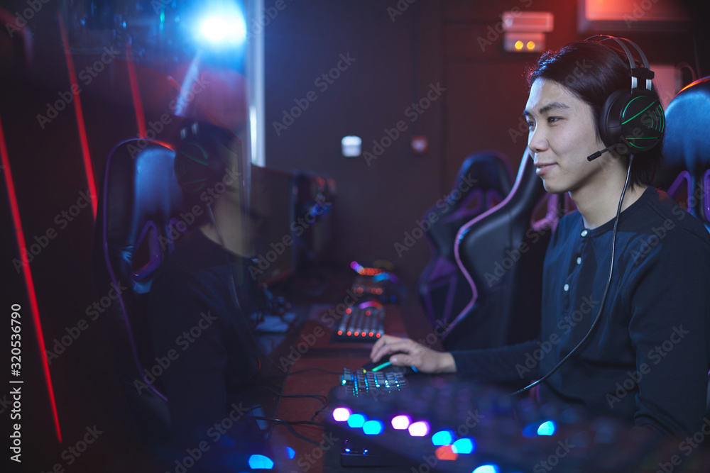 Side view portrait of smiling Asian pro-gamer enjoying videogames in computer studio, copy space