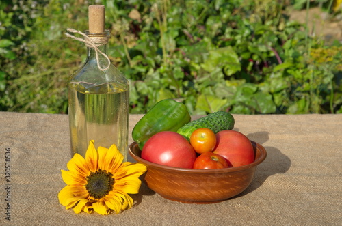 A bottle of sunflower oil and fresh vegetables on the table in the garden