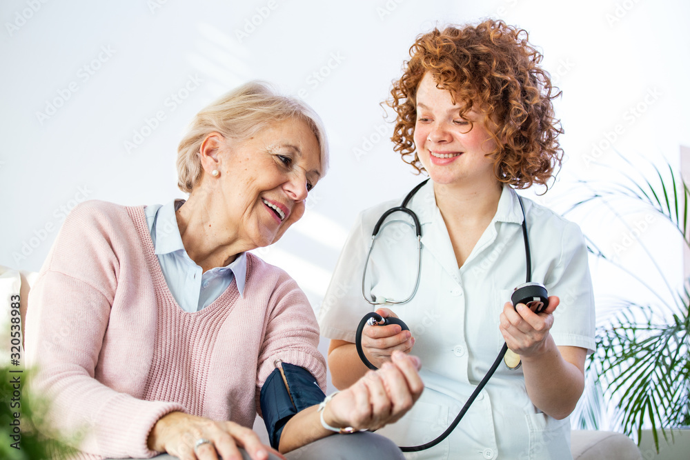 Young nurse measuring blood pressure of elderly woman at home. Female nurse checking blood pressure of a senior woman at home,Home carer checking patients blood pressure Young nurse measuring blood pressure of elderly woman at home. Female nurse checking blood pressure of a senior woman at home,Home carer checking patients blood pressure