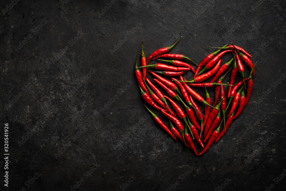 Spicy red chili pepper in the shape of a heart on a dark stone background, design concept for Valentine's day