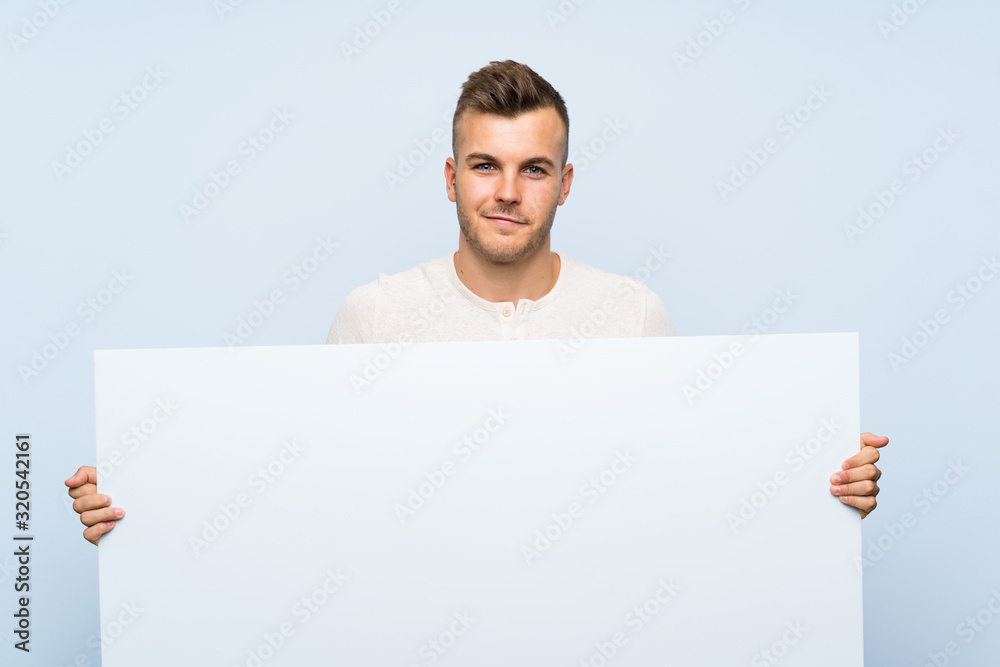 Young handsome blonde man over isolated blue background holding an empty white placard for insert a concept Young handsome blonde man over isolated blue background holding an empty white placard for insert a concept