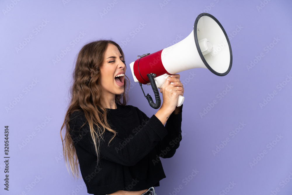 Young woman over isolated purple background shouting through a megaphone Young woman over isolated purple background shouting through a megaphone
