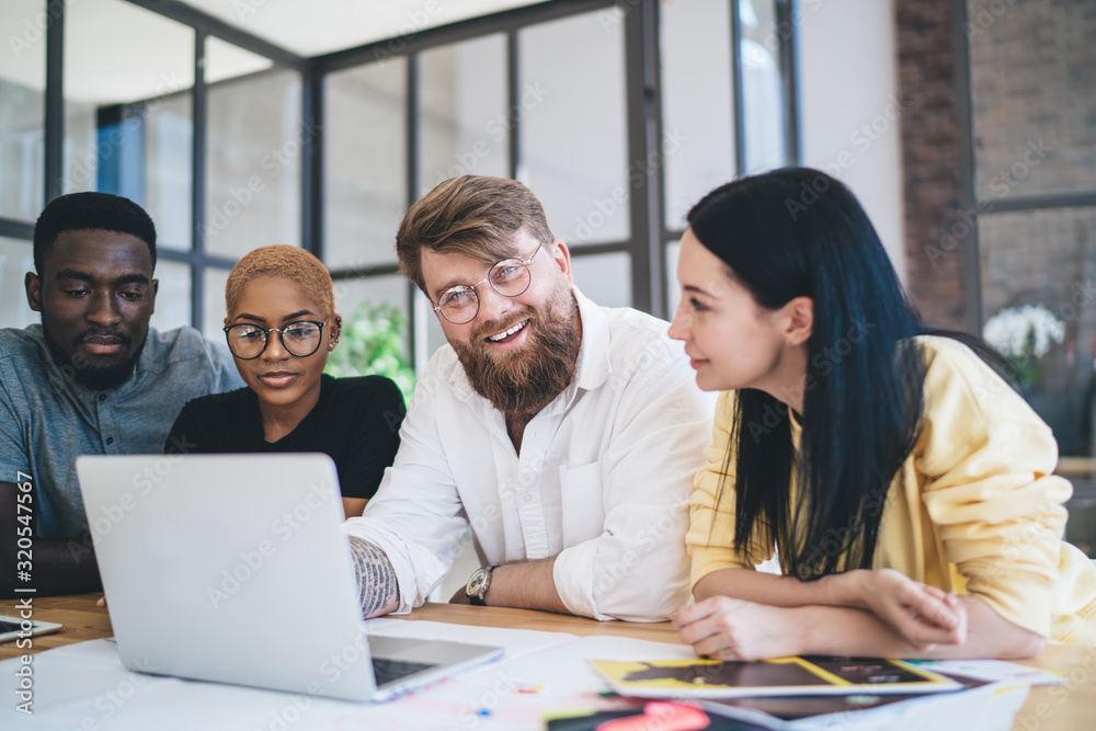 Fototapeta premium Cheerful confident diverse people using laptop while having discussion