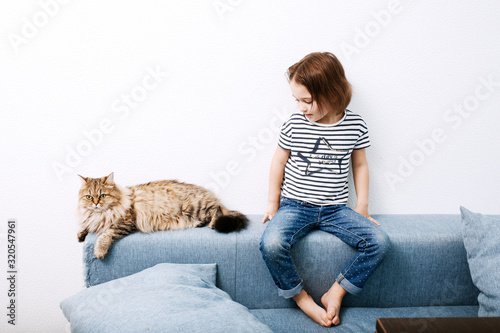 Obraz na płótnie Little preschooler girl child sitting on a couch with cat against white wall background w salonie