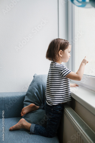 Little bored brunette girl sitting at home and looking at the window