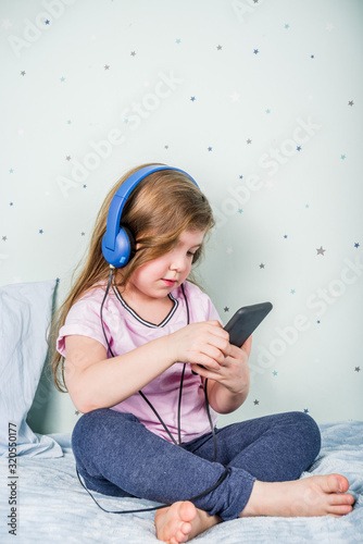 Kids Gaming video games concept. Toddler or young girl, playing game with joystick, smart-phone, VR glasses and headphones, enjoying games, sitting on sofa in living room at home.