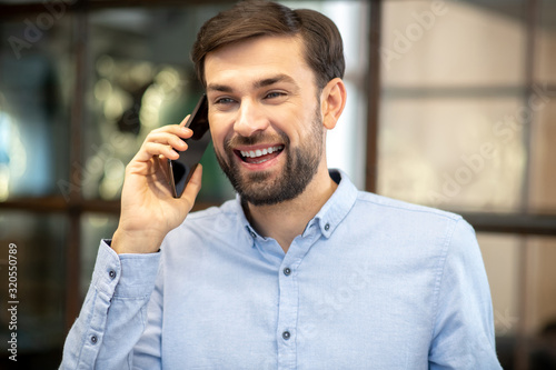 Young bearded man in a blue shirt talking on the phone and feeling awesome