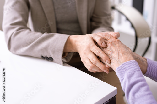 Close-up of unrecognizable social worker holding hands of elderly woman while supporting her