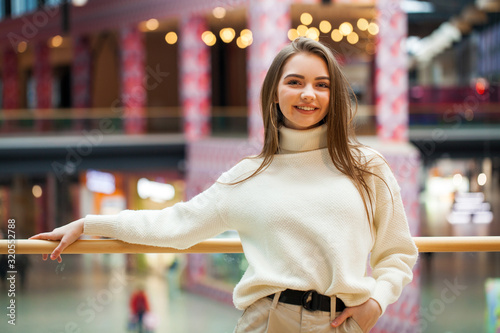 Portrait of a young beautiful woman in beige sweater and pants posing in the mall