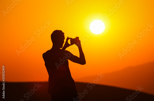 Silhouette of a man photographing a sunset on the phone on the background of a golden sun