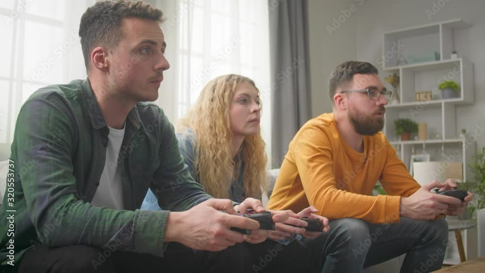 Three friends play video games while sitting on a couch in a living room Three friends play video games while sitting on a couch in a living room