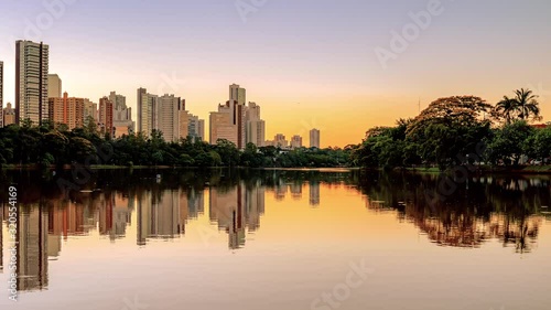 View of a city lake on a beautiful sunset. Lake shore with a green area of trees, and few buildings of the city on background. Video of Igapo lake at Londrina PR Brazil.
