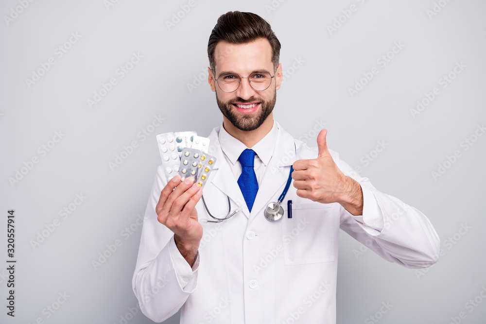 Close-up portrait of nice attractive glad cheerful doc holding in hands plates of pills excellent therapy treatment positive effect showing thumbup isolated on light white gray pastel color background Close-up portrait of nice attractive glad cheerful doc holding in hands plates of pills excellent therapy treatment positive effect showing thumbup isolated on light white gray pastel color background