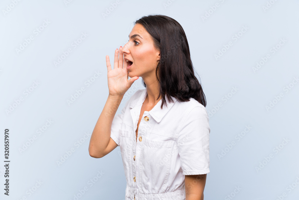 Young woman over isolated blue background shouting with mouth wide open Young woman over isolated blue background shouting with mouth wide open