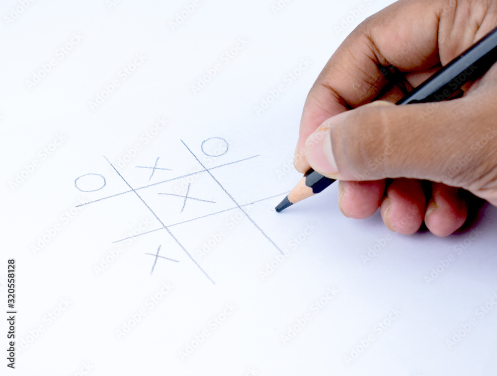 A person playing tic tac toe on a white paper with a black wood pencil in his hand A person playing tic tac toe on a white paper with a black wood pencil in his hand