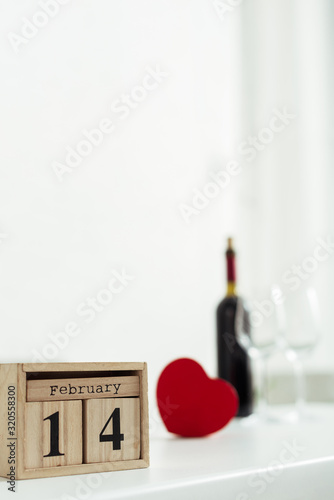 selective focus of wooden cubes with 14 february lettering near bottle of wine and glasses