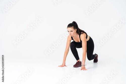 Female athlete in position to start running - isolated over a white background.