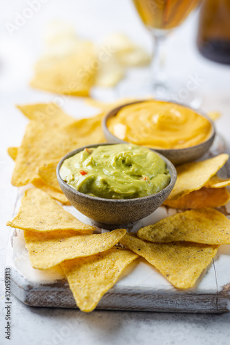 Nachos chips in a bowl with sauces guacamole and cheese, dip variety, over white stone background.