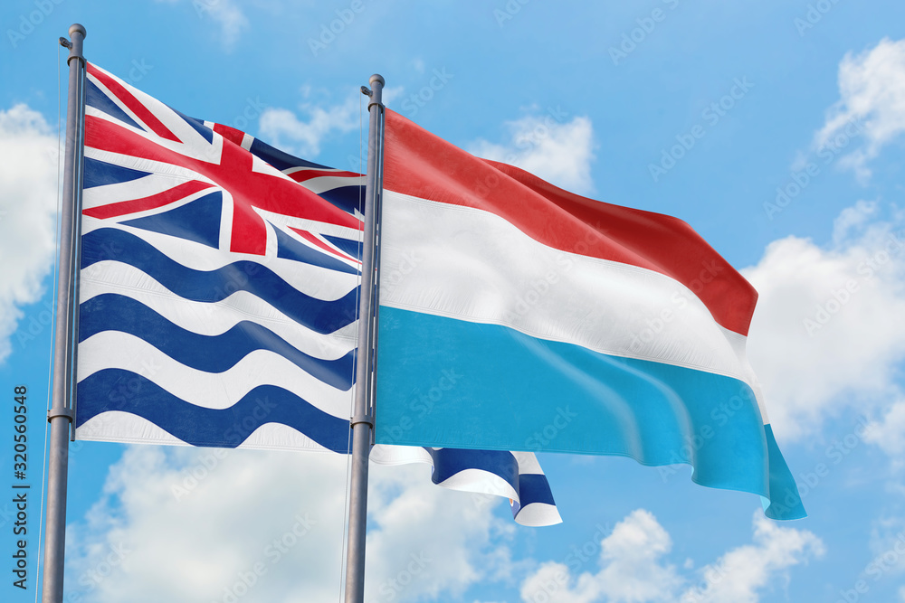 Luxembourg and British Indian Ocean Territory flags waving in the wind against white cloudy blue sky together. Diplomacy concept, international relations.