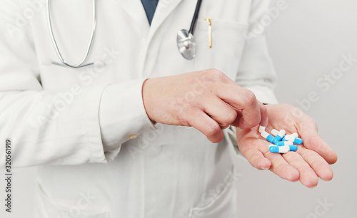 Cropped image of unrecognizable doctor having handful of blue and white gelatin capsules trying to take one