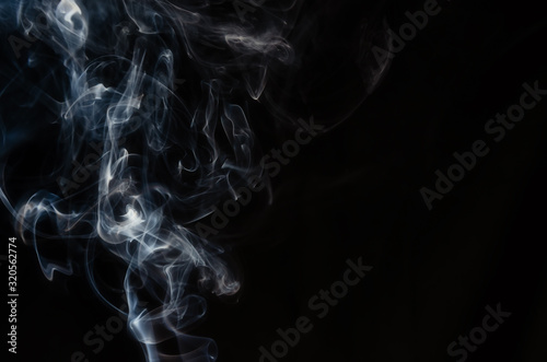 Abstract figure made of smoke on the left side of the frame on a dark background with place for text.