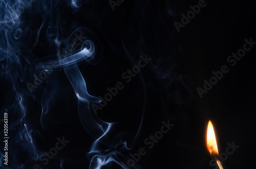 Fototapeta Naklejka Na Ścianę i Meble -  Fire with an abstract figure from blue smoke on a dark background with a place for text, fantasy,fiction, mysticism, magic.