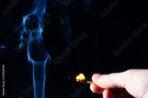 Smoke abstract figure on the left side of the frame and a hand with a burning match on the right side of the frame.