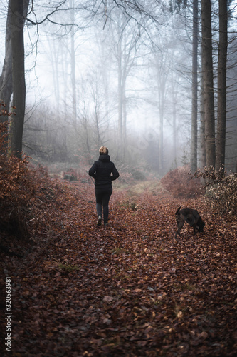 Frau und Hund spazieren durch einen Wald der im Nebel liegt © ramonmaesfotografie