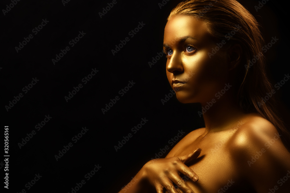 Fashion art Golden skin Woman face portrait metal skin, model in gold make-up. Beauty fashionable girl model with golden make-up on black background. Beauty model golden make-up on black background.