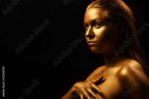 Fashion art Golden skin Woman face portrait metal skin, model in gold make-up. Beauty fashionable girl model with golden make-up on black background. Beauty model golden make-up on black background.