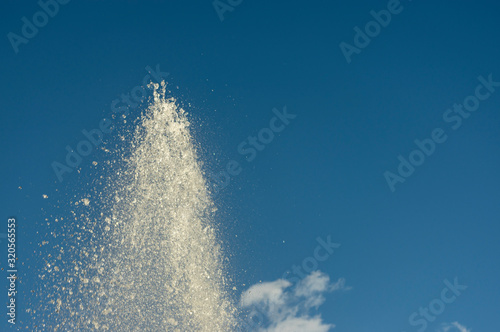 Spitze einer Wasserfont  ne eines Springbrunnens bei strahlendem Sonnenschein gegen blauen Himmel mit kleinen wei  en Wolken