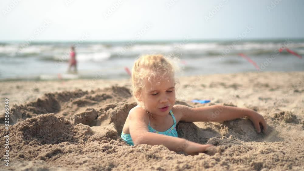 5 years old girl buried in sand break free and run away. Blurred people and sea 5 years old girl buried in sand break free and run away. Blurred people and sea