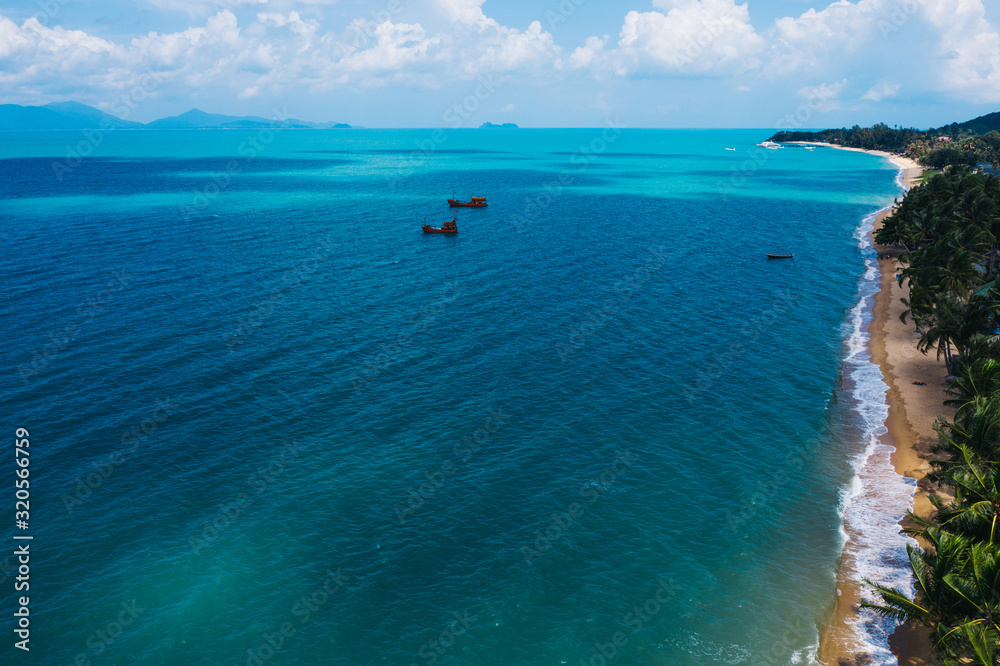 Obraz premium Aerial scenery view of white sand beach shore with turquoise clear sea water and foamy waves. Bird's eye panoramic view of picturesque coastline bay with big fishermen boats. Samui island, Thailand