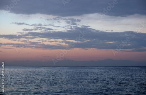 Twilight view on high mountain silhouettes with white snow caps on tops far away on horizon after the sea under sky with beautiful clouds