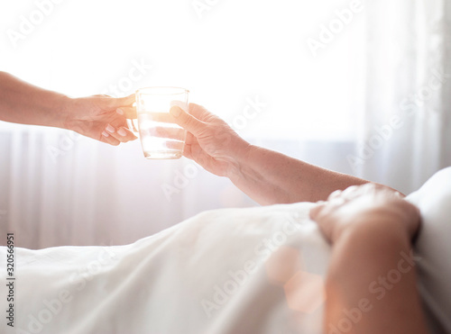 Social worker gives an elderly woman a disabled person a mug of water on a background of a window with the sun. The concept of care for the elderly and disabled, service, copy space