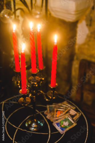 Burning red candles on a fortune-telling table with cards and a triquetre sign.