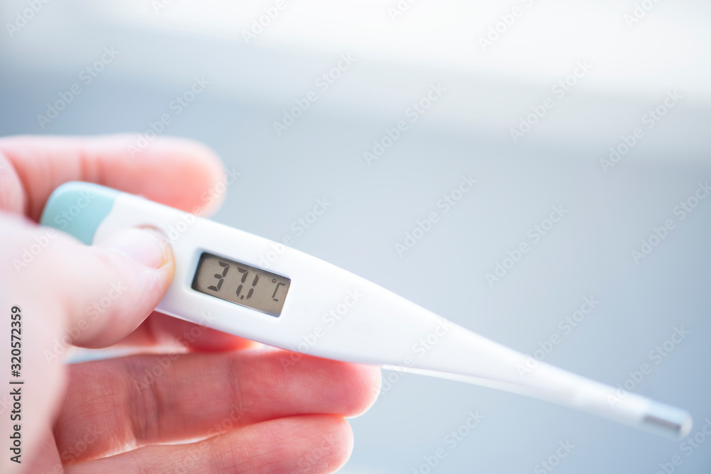Female hand holds an electronic thermometer on a bokeh background. Female hand holds an electronic thermometer on a bokeh background.