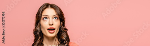 panoramic shot of surprised young woman looking up isolated on pink