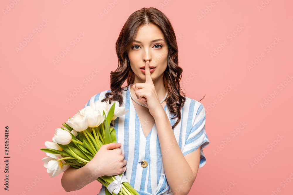 serious girl showing hush sign while holding bouquet of white tulips isolated on pink serious girl showing hush sign while holding bouquet of white tulips isolated on pink