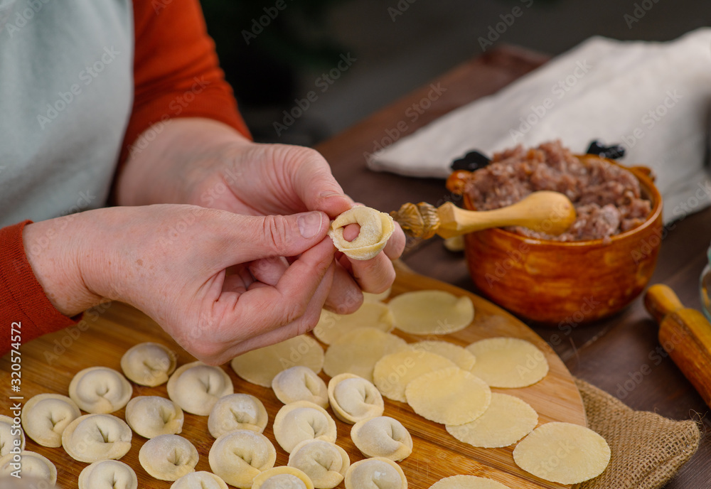Woman cook sculpts dumplings with his hands, close-up. On the table is minced meat and rolled circles of dough