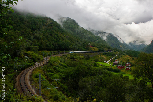 The railway in the Norwegian valley from the city of Flåm to Myrdal station. A train arriving at the station is visible in the distance