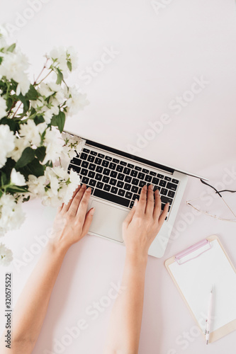 Woman working on laptop. Office desk workspace with computer, flowers bouquet and stationery on pink table. Flat lay, top view business hero header background.